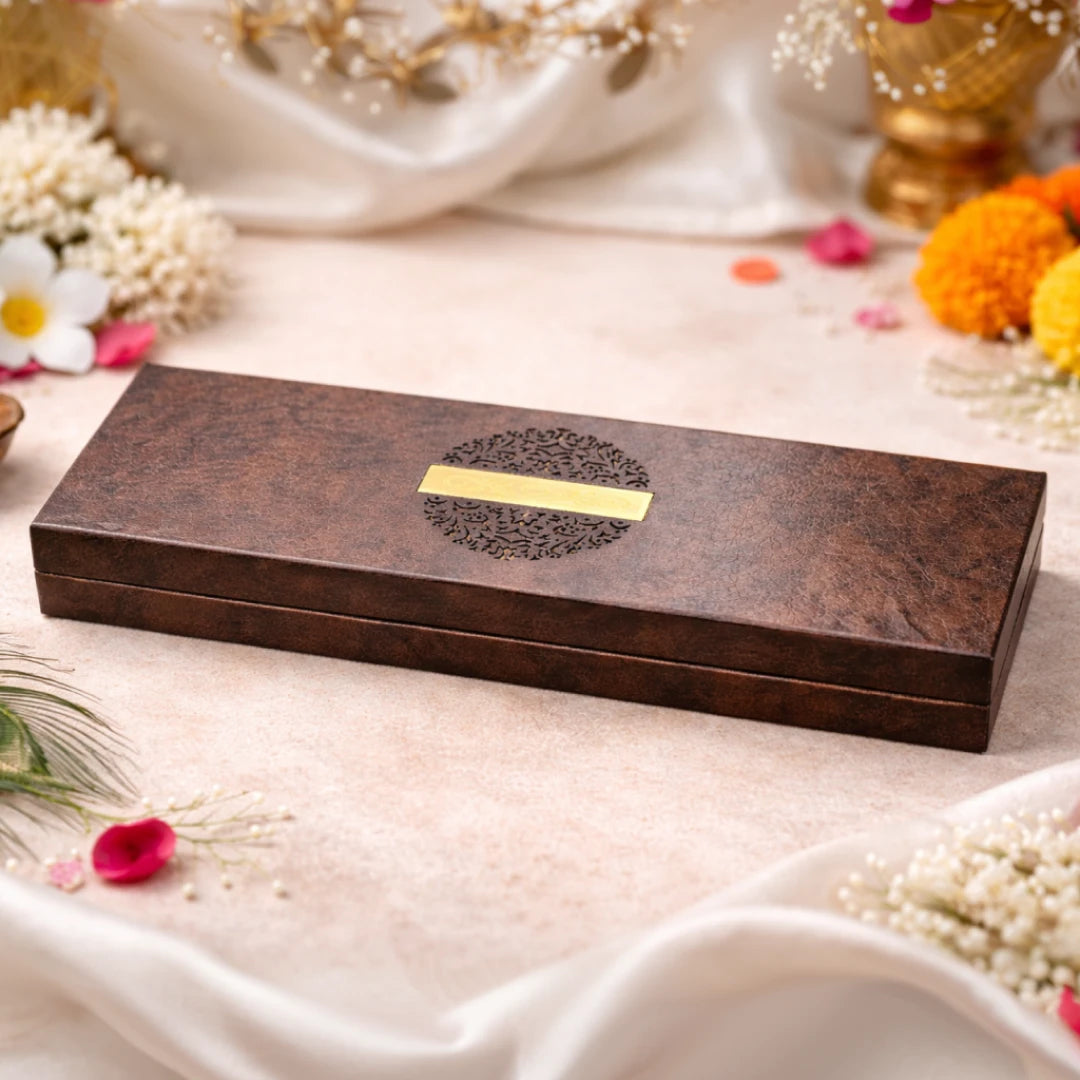 Open mahogany wooden keeper box for the Karungali Trishul Mala — two Maha Mrityunjay Yantras built into the inner lid, mala with silver Trishul pendant resting below on black velvet, surrounded by marigold flowers, jasmine and brass diyas
