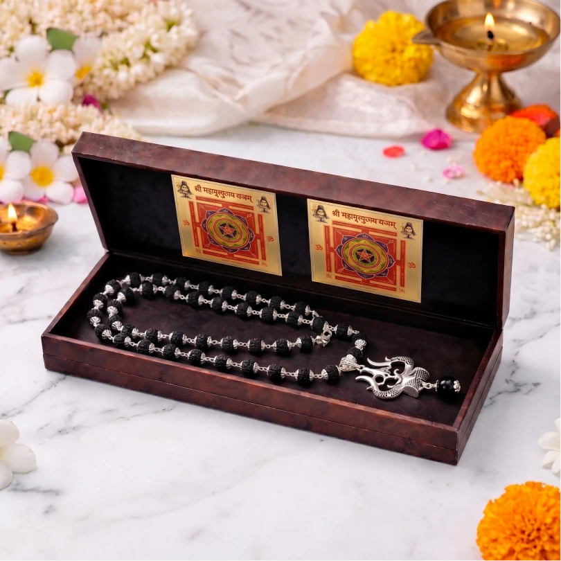 Karungali Mala with silver Trishul OM pendant displayed on dark wood with rice grains and marigold petals — Shubh Darshan Kashi Siddh certified product hero image